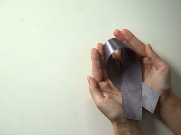 Image shows two open hands holding a gray cancer ribbon in their palms