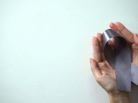 Two open hands holding a gray cancer ribbon in their palms