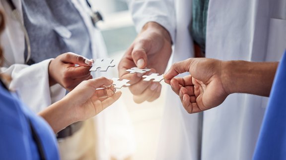 Doctors holding up puzzle pieces; representing working together